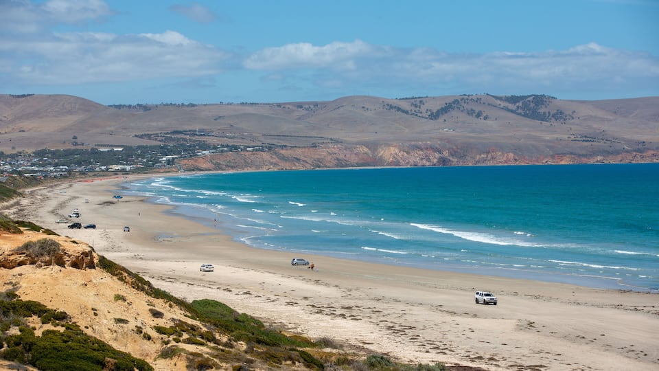 A coastal landscape with a beach, ocean, and distant hills.