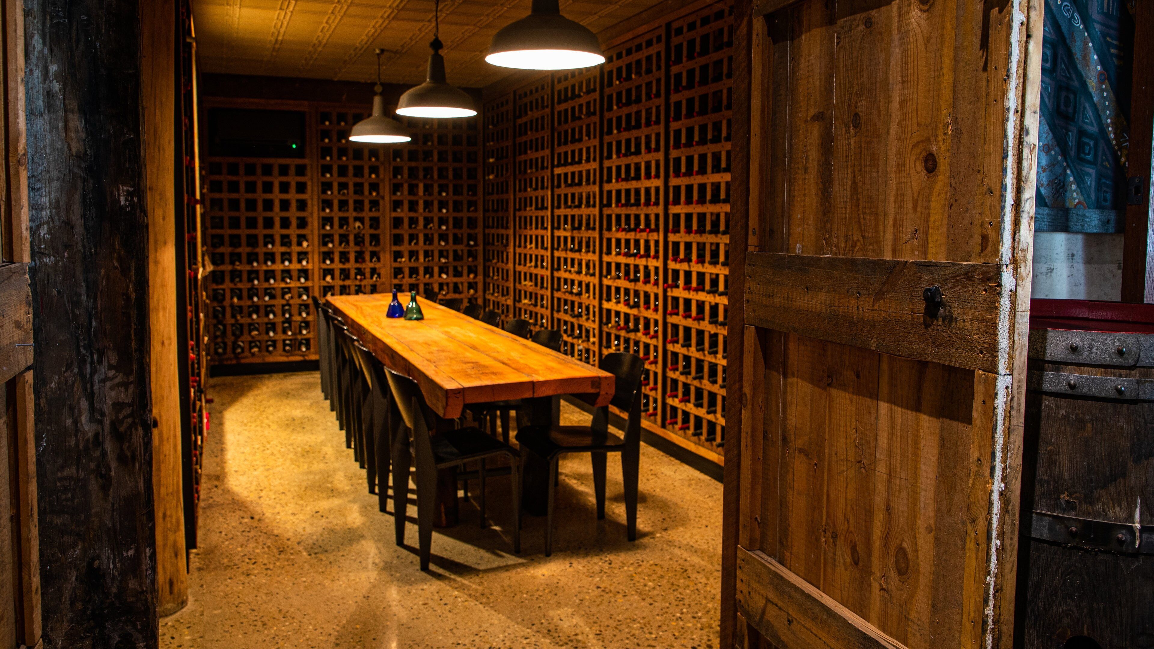 A wooden wine cellar with a long table and chairs, and a wall of wine racks.