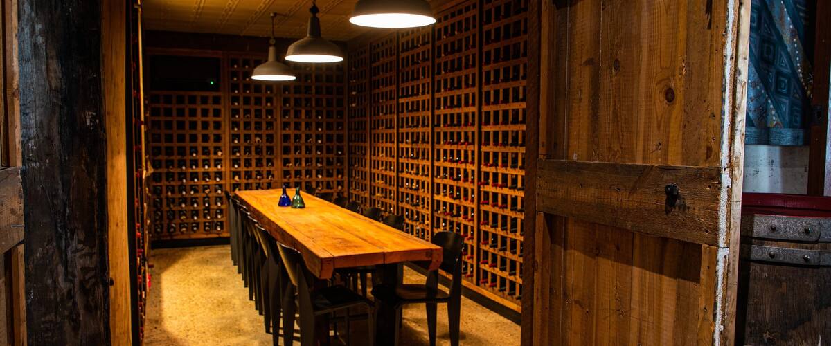A wooden wine cellar with a long table and chairs, and a wall of wine racks.
