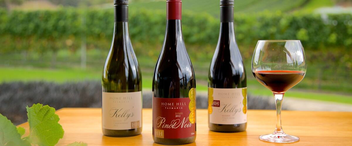Three wine bottles and a wine glass on a table with a vineyard in the background.