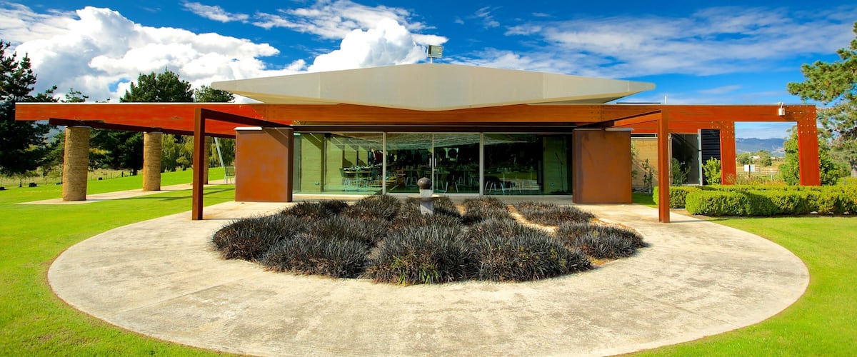 A modern building with a glass facade, surrounded by a circular garden and red beams.