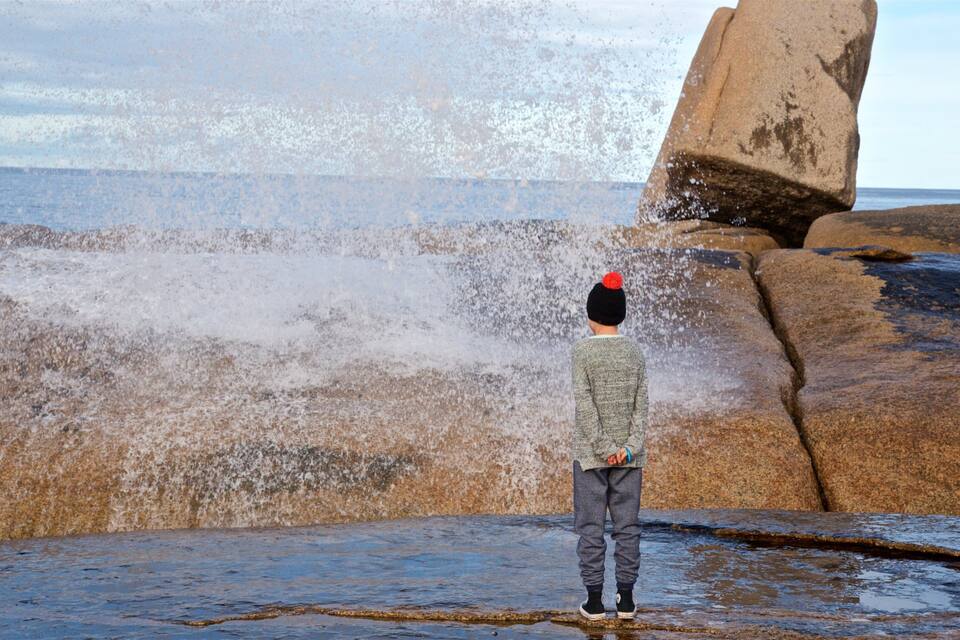 A person standing on a rocky shore with waves crashing against the rocks.