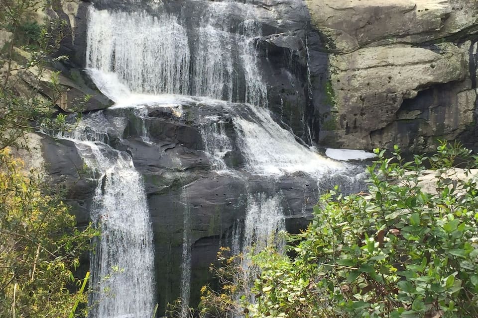 Ein mehrstufiger Wasserfall stürzt über felsiges Gelände, umgeben von üppiger Vegetation.
