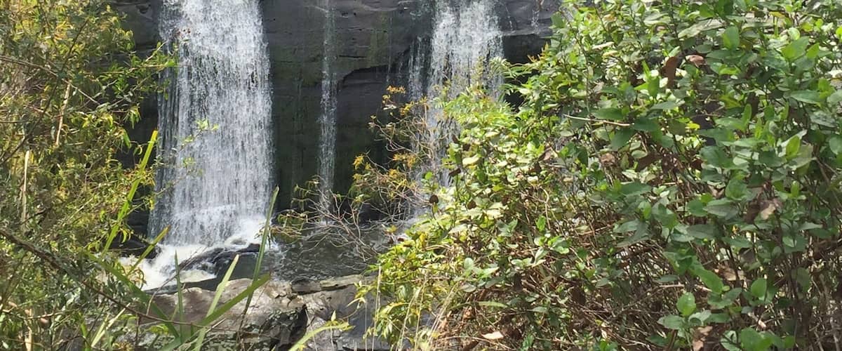 A multi-tiered waterfall cascading over rocky terrain surrounded by lush greenery.