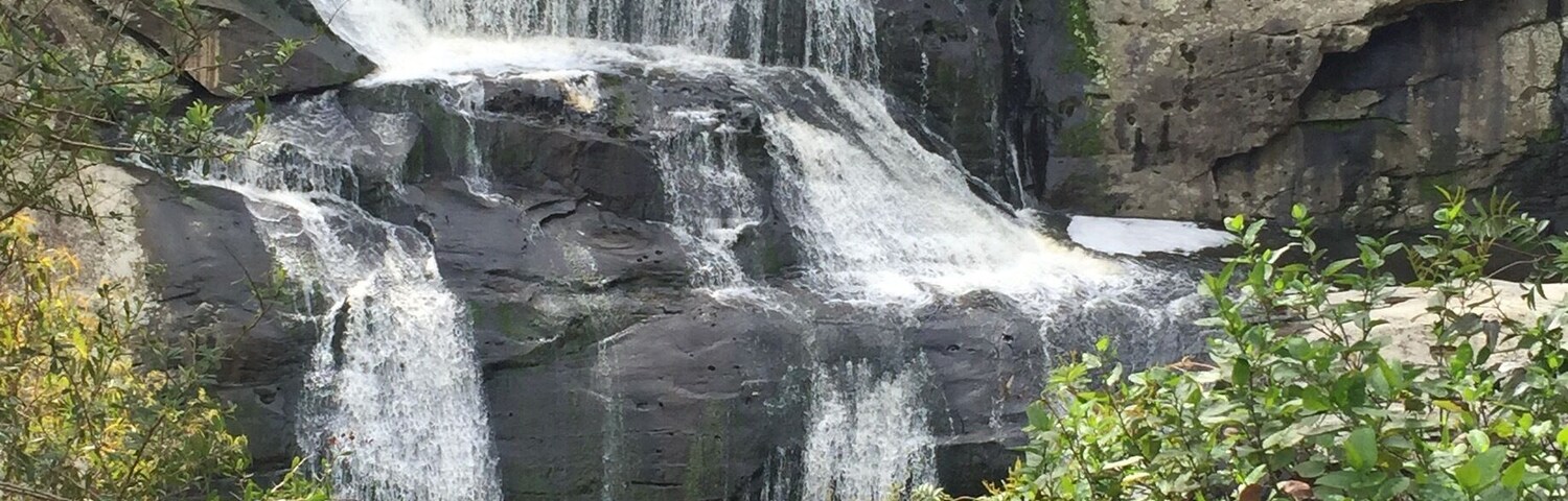 A multi-tiered waterfall cascading over rocky terrain surrounded by lush greenery.