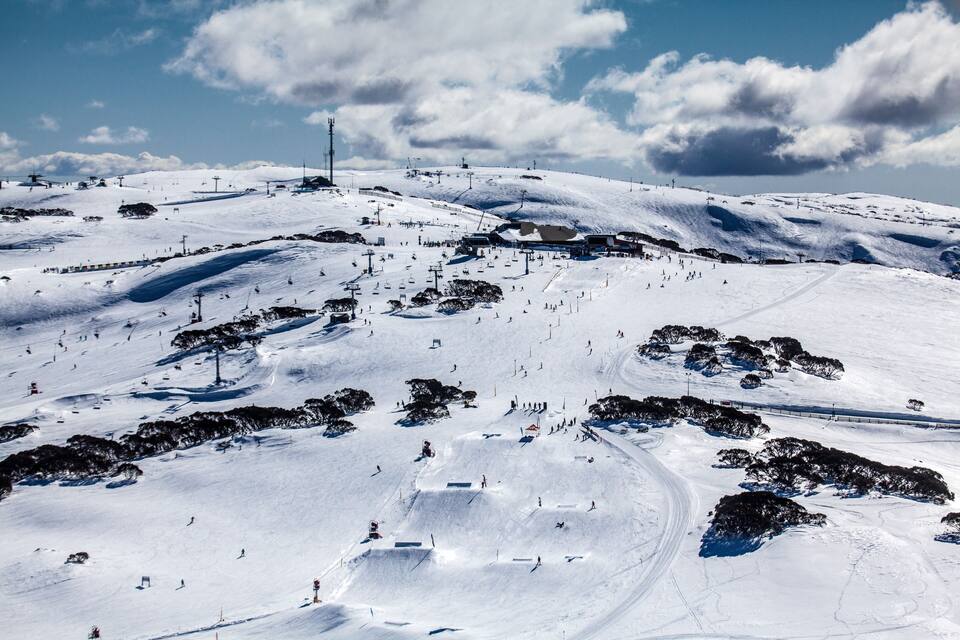 Een met sneeuw bedekte piste met skiliften, bomen en een heldere lucht.