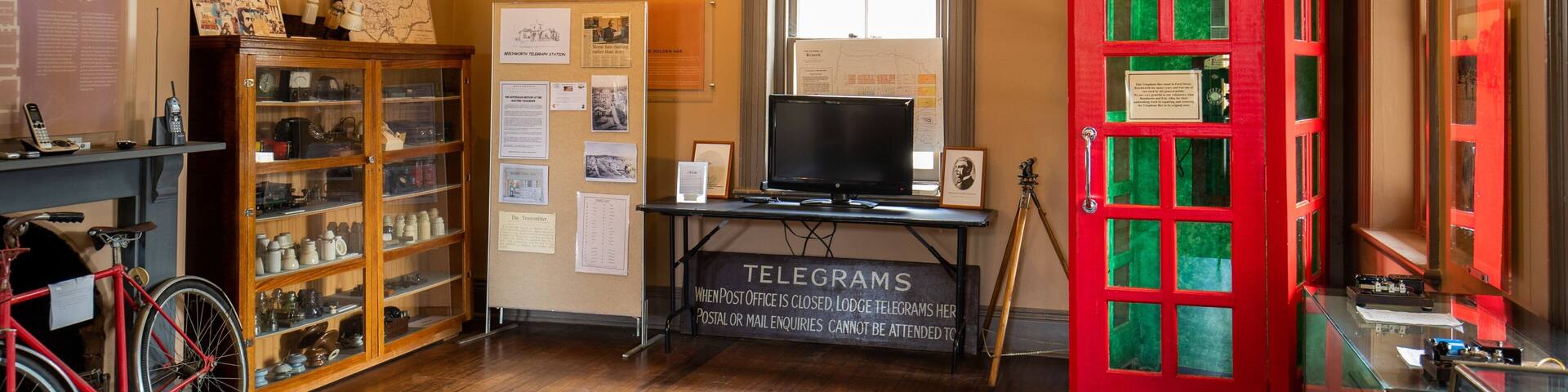 A vintage telegraph office with a red telephone booth, wooden cabinets, and a bicycle.