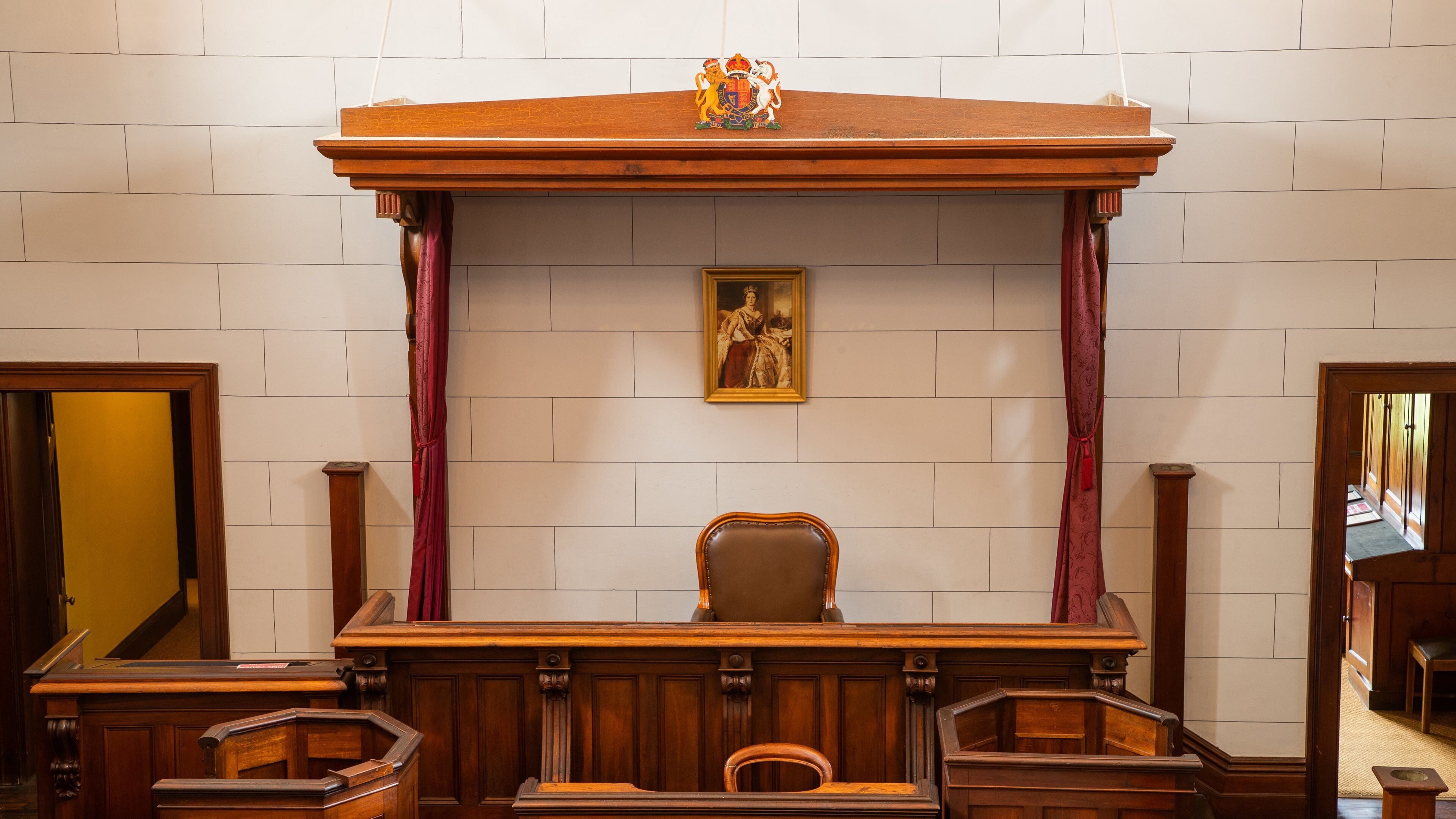 A courtroom with a wooden bench, judge's chair, and a coat of arms above the bench.