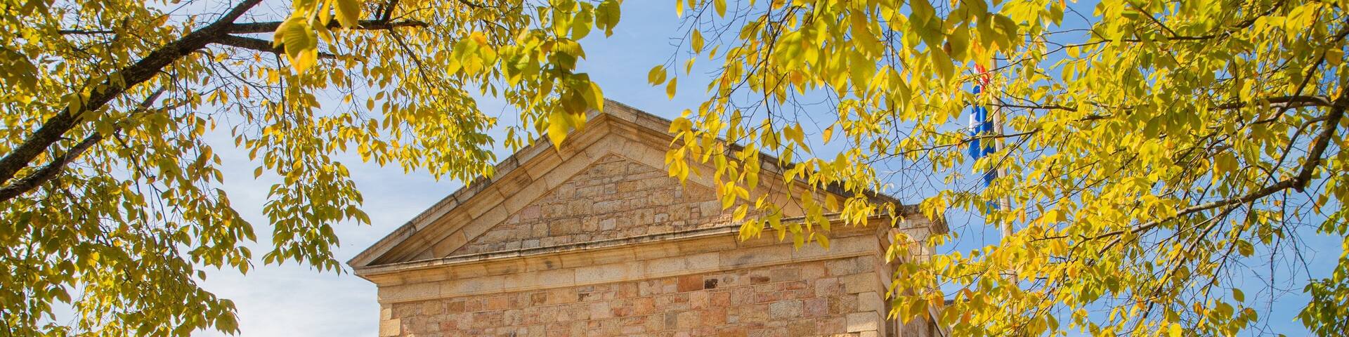 A stone building with a pitched roof, surrounded by trees with yellow leaves.