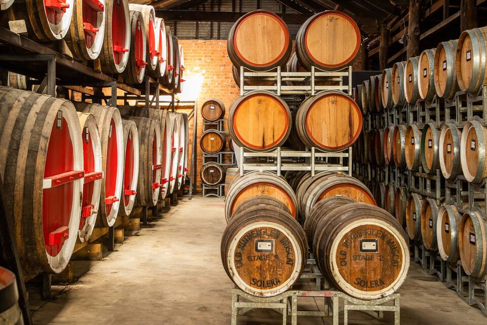 Des tonneaux en bois, remplis de vin, sont empilés dans un entrepôt.