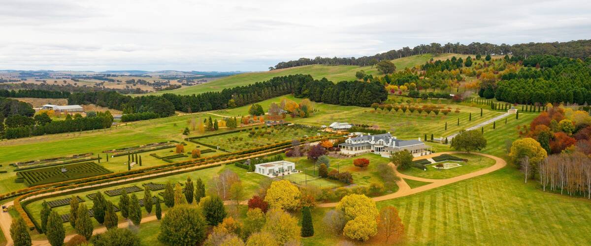 A large estate with manicured gardens, a formal lawn, and a variety of trees in autumn colors.