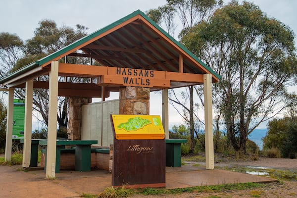 Une structure en bois portant l’inscription « Hassans Walls », avec un panneau indiquant un point sur la carte et un banc.
