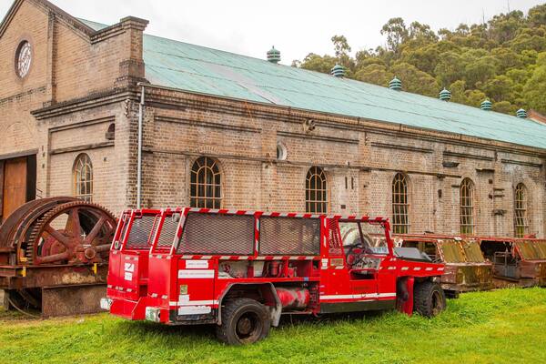 A red truck parked in front of a large brick building with a green roof.