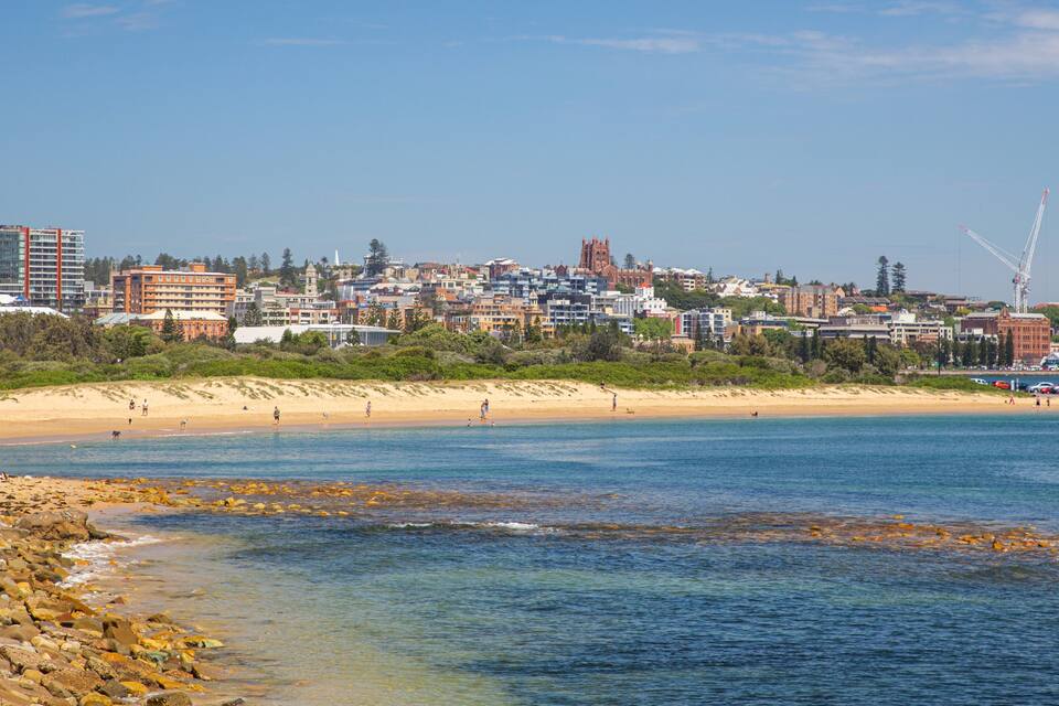 A coastal cityscape with a sandy beach, rocky shoreline, and a variety of buildings including residential and commercial structures.