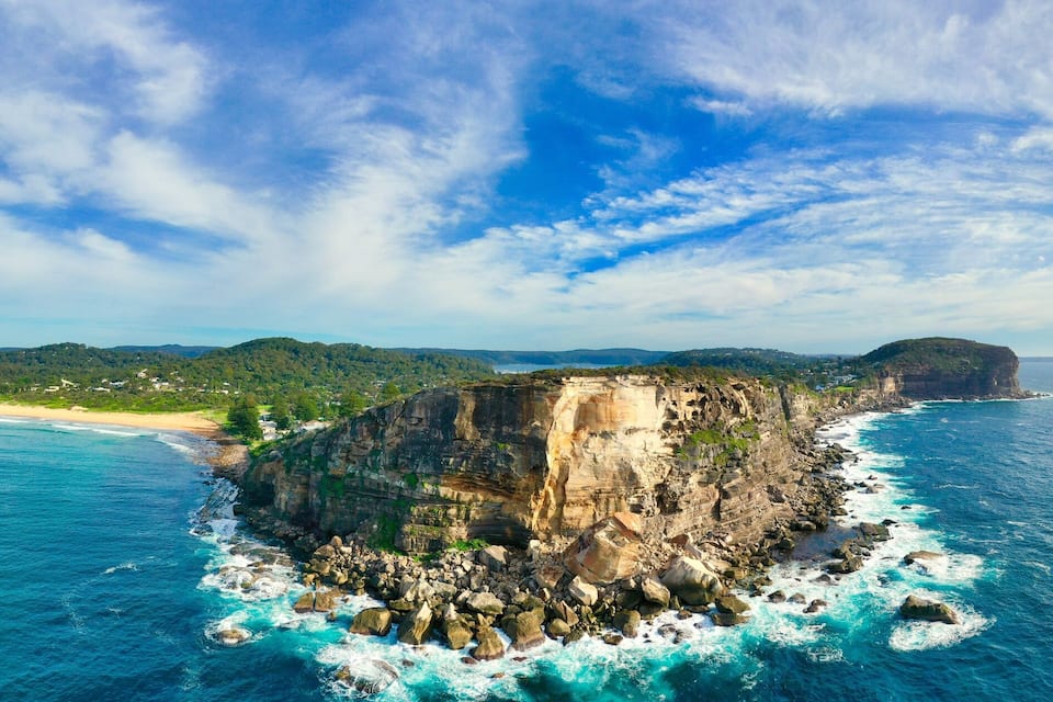 A coastal landscape with a prominent rocky cliff, a beach, and distant hills.