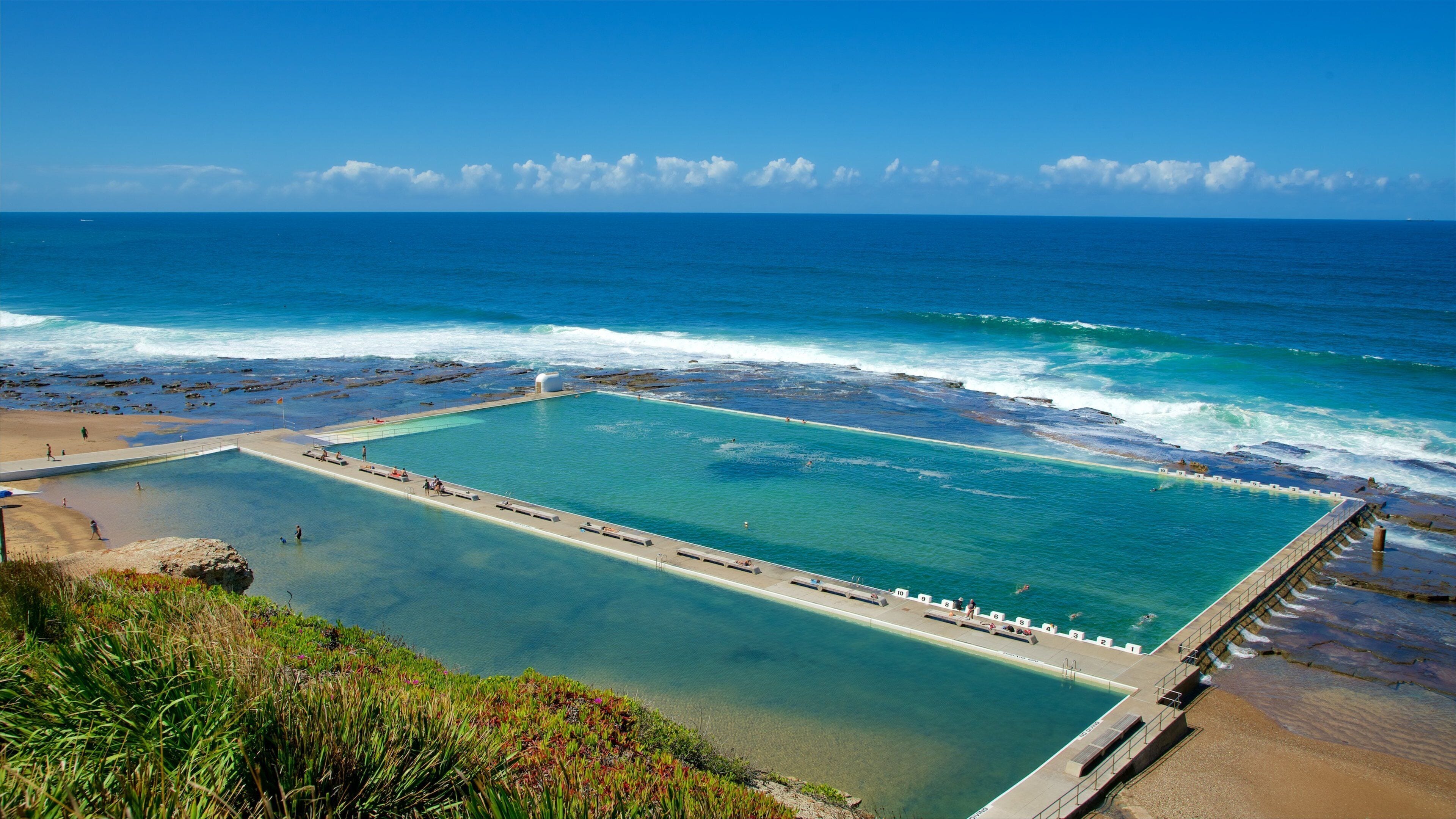 Ein Küsten-Schwimmbecken mit klarem, blauem Wasser, umgeben von einer felsigen Küstenlinie und einem Sandstrand.
