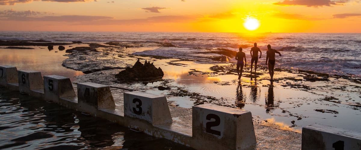Merewether Ocean Baths which includes a sunset and general coastal views as well as a small group of people
