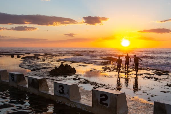 Merewether Ocean Baths which includes a sunset and general coastal views as well as a small group of people