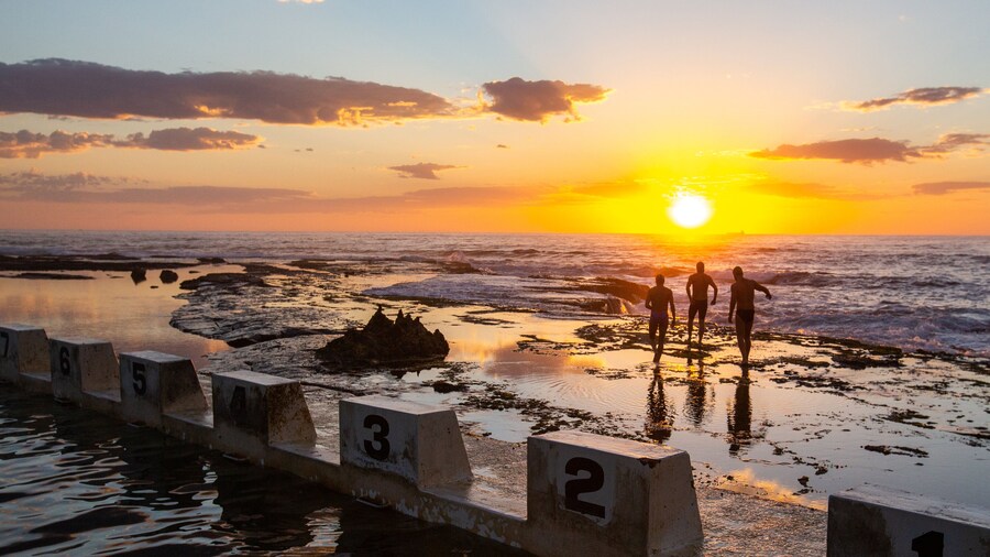 Merewether Ocean Baths which includes a sunset and general coastal views as well as a small group of people