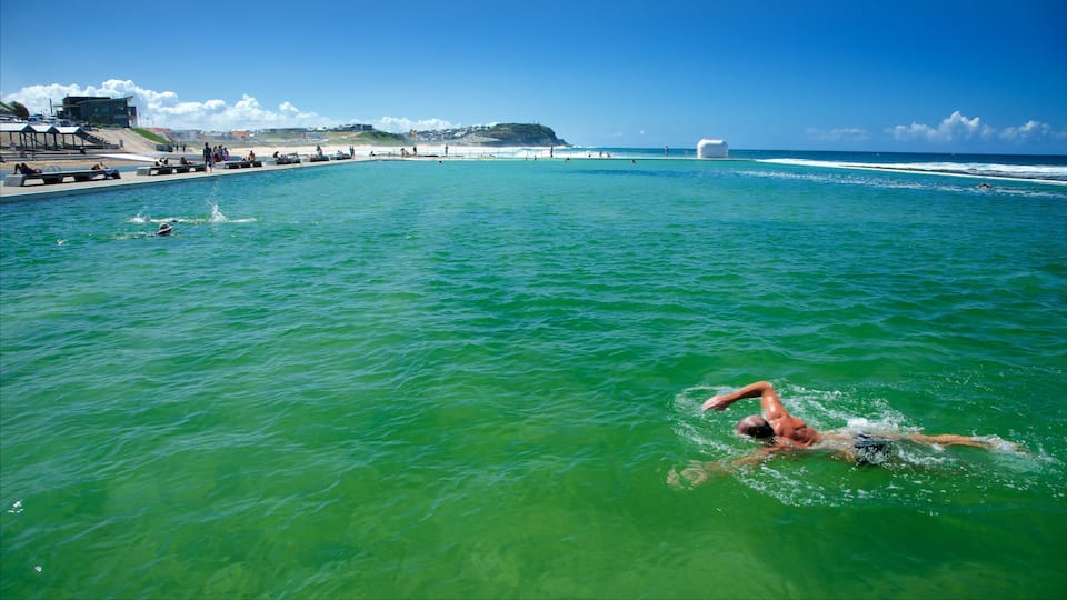 Nadador en el océano, con una playa y edificios al fondo.
