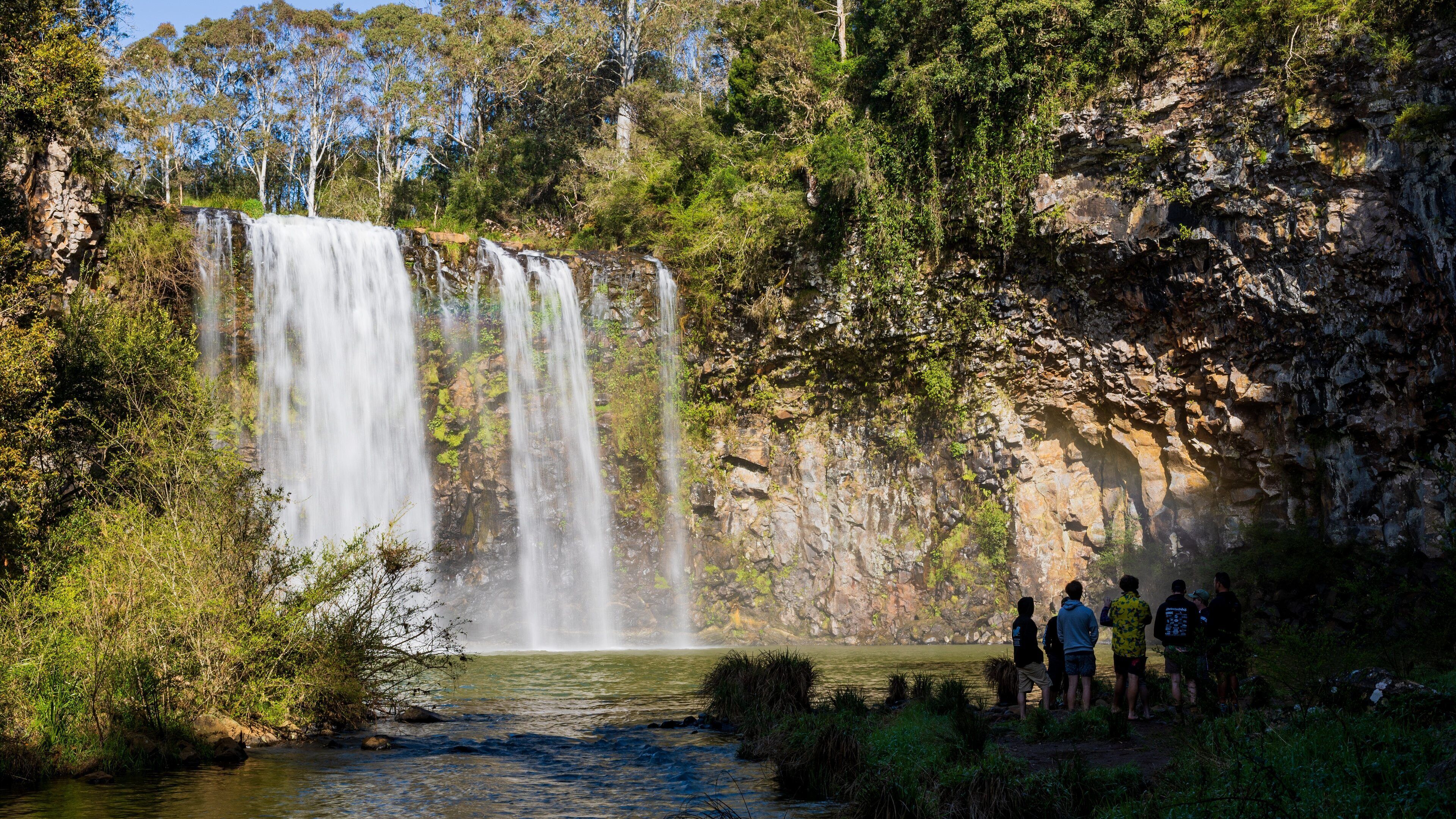 A waterfall cascading into a river surrounded by lush greenery and rocky cliffs.