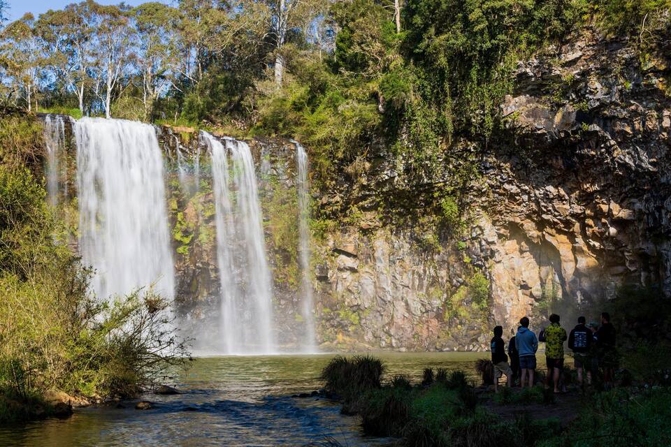 A waterfall cascading into a river surrounded by lush greenery and rocky cliffs.