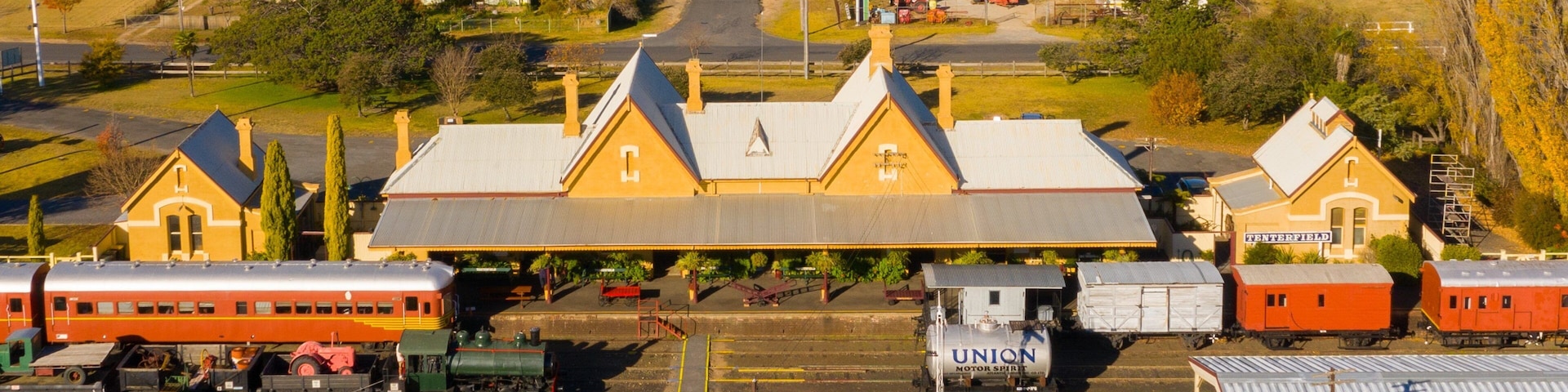 Una estación de tren con un edificio amarillo grande, varias vías y zonas residenciales aledañas.