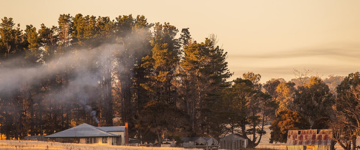 A rural landscape with a house, barns, and a forest.