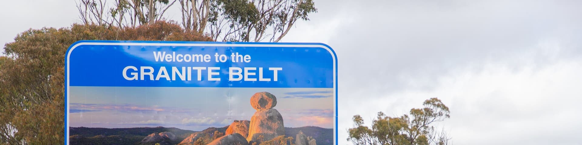 A road sign welcoming visitors to the Granite Belt with a scenic landscape.