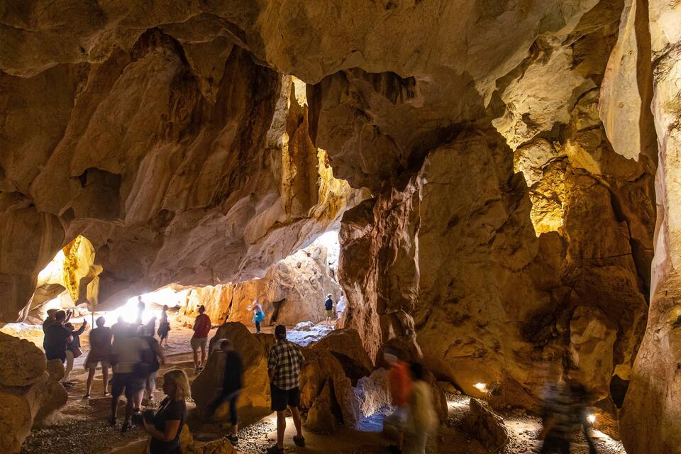 Una cueva con estalactitas y estalagmitas, iluminada con luz artificial.