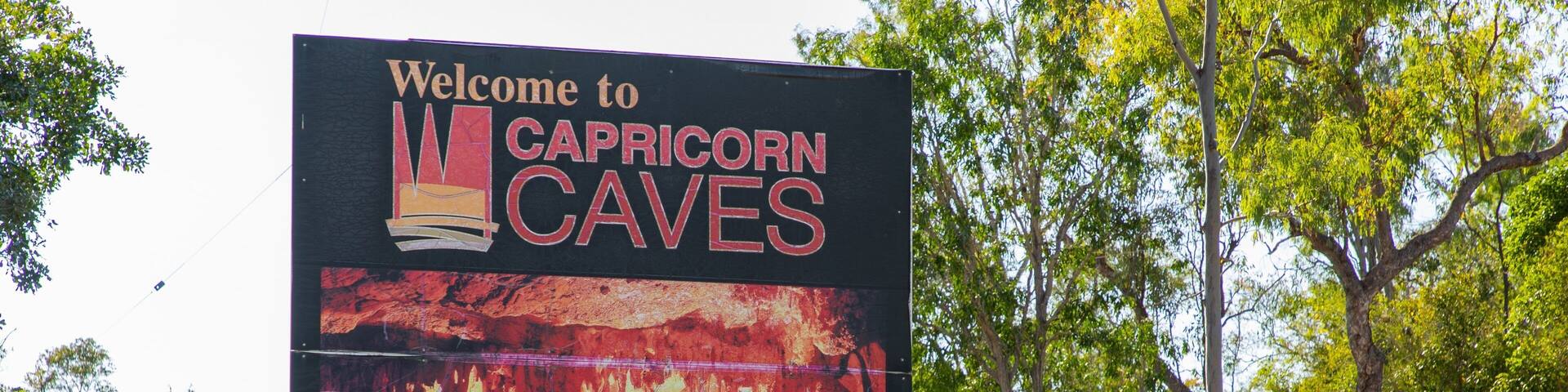 A sign welcoming visitors to Capricorn Caves, with gates open from 8:30 am to 6:00 pm, and a 'Sorry No Pets' notice.