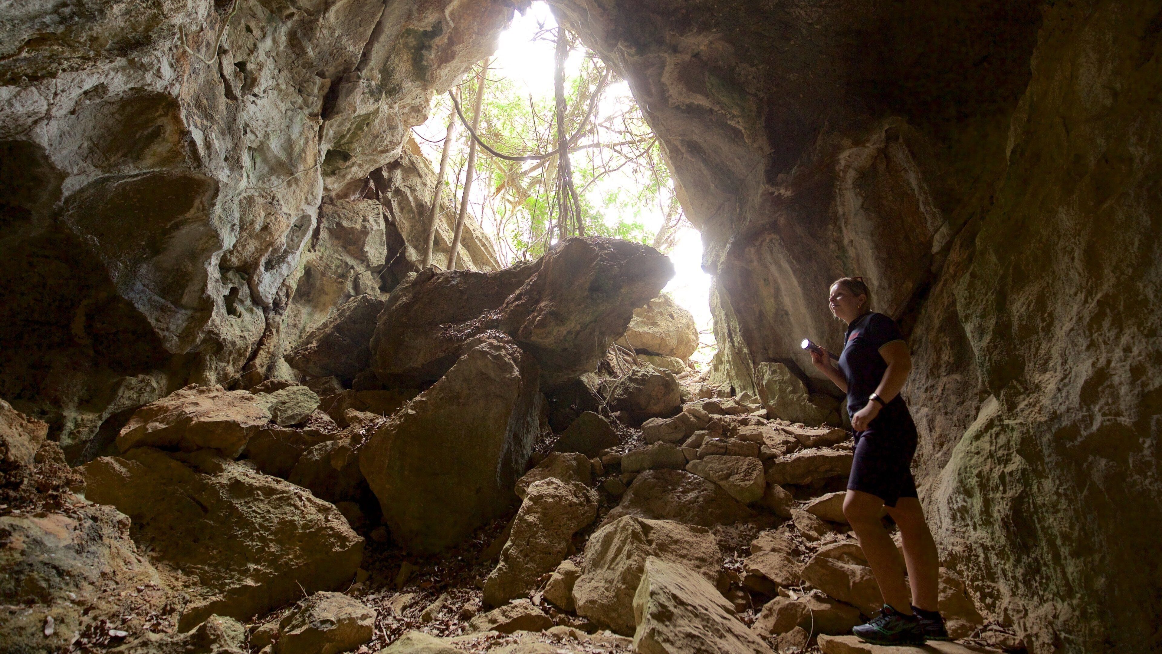 A person exploring a rocky cave with sunlight streaming through an opening.