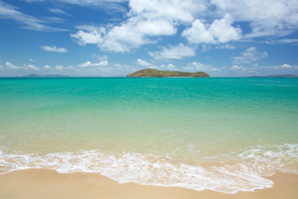 A beach with clear turquoise water, a sandy shore, and a small island in the distance.