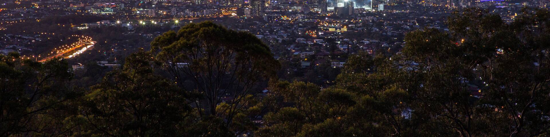 A cityscape at dusk with illuminated buildings and a sunset sky.