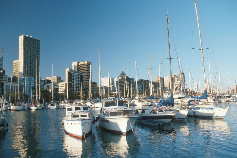 A marina with numerous sailboats docked, surrounded by tall buildings.