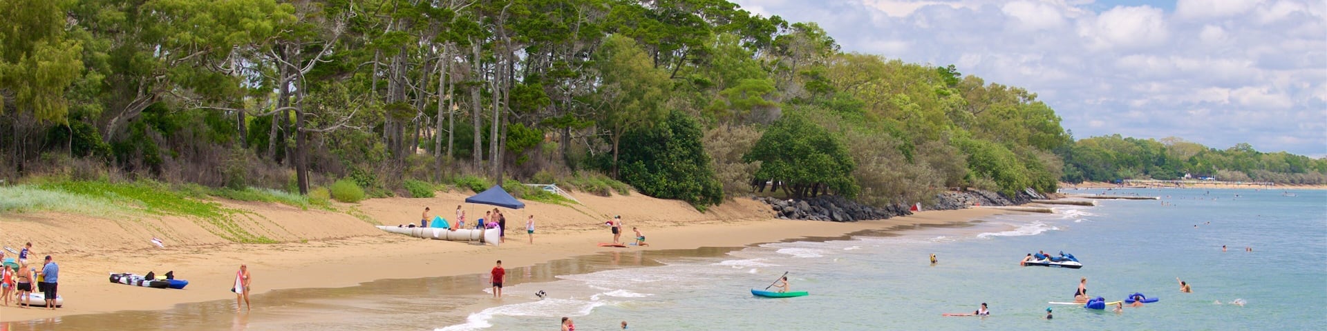 A beach with people swimming, paddling in boats, and sunbathing.