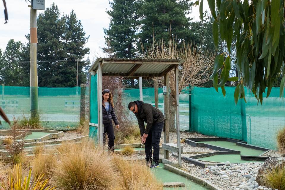 A golf course with a green netted area, a wooden shelter, and a person in a black jacket.