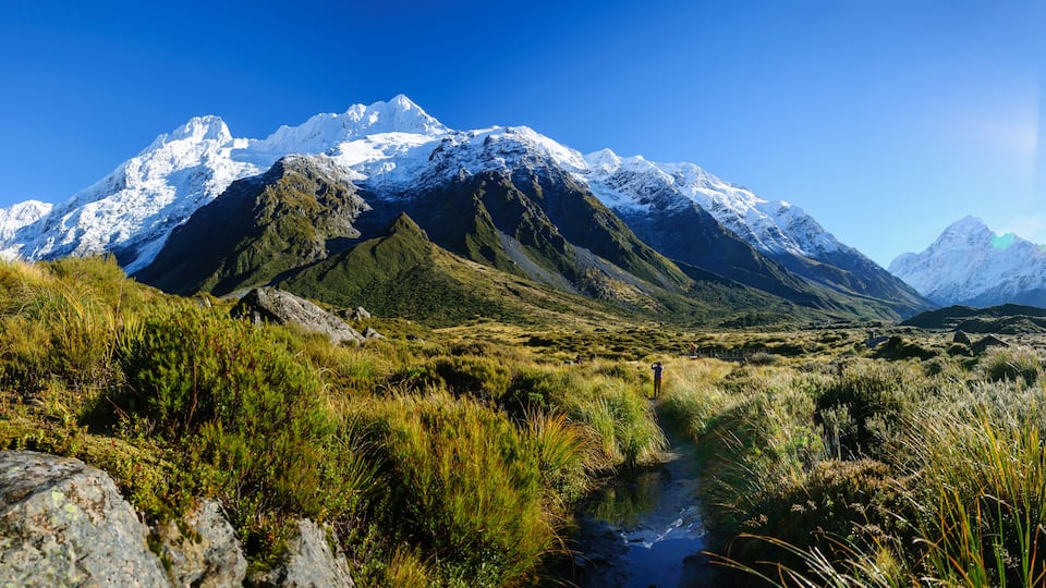 A mountainous landscape with a stream, rocky terrain, and lush greenery.