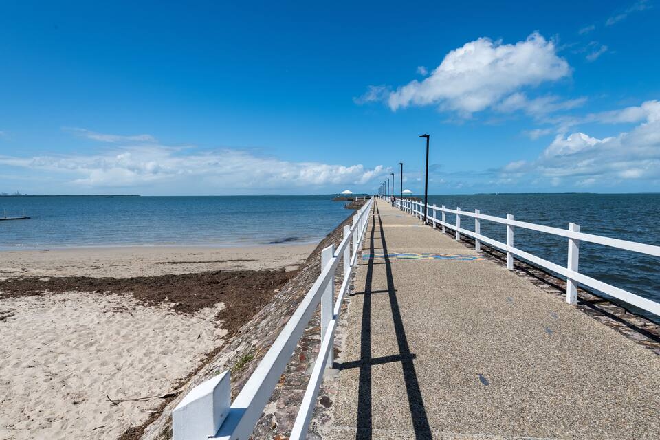 A coastal walkway with a white railing, leading to a sandy beach and the ocean.