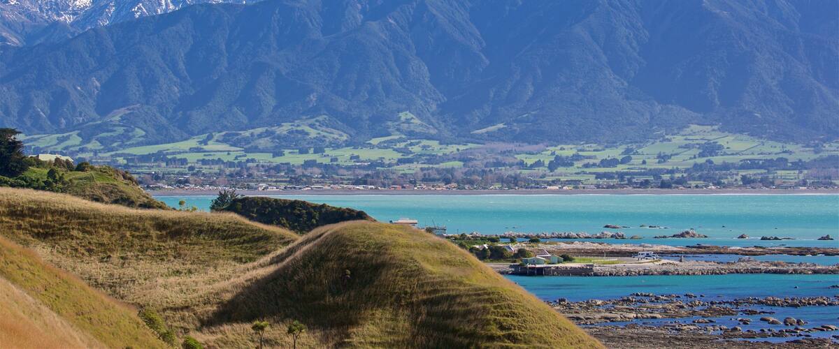 A coastal landscape with mountains in the background and a turquoise sea in the foreground.