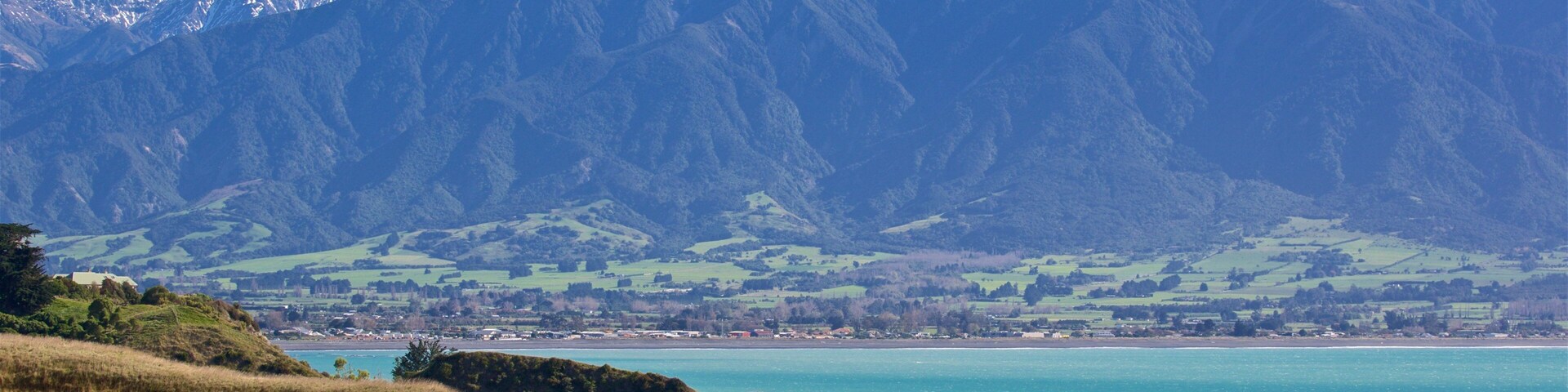 A coastal landscape with mountains in the background and a turquoise sea in the foreground.