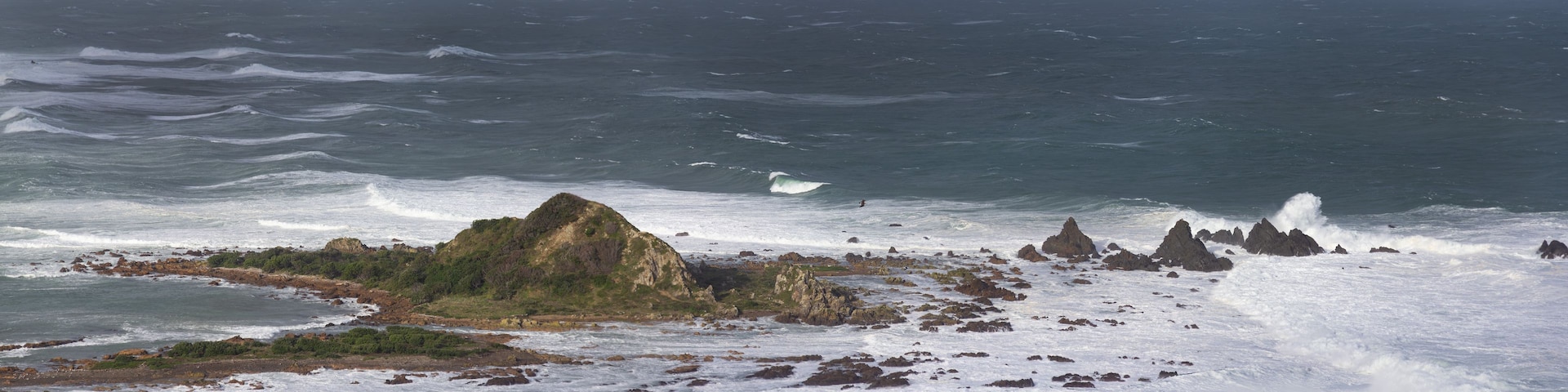 Une côte accidentée, parsemée de formations rocheuses, où les vagues viennent s’écraser avec force.