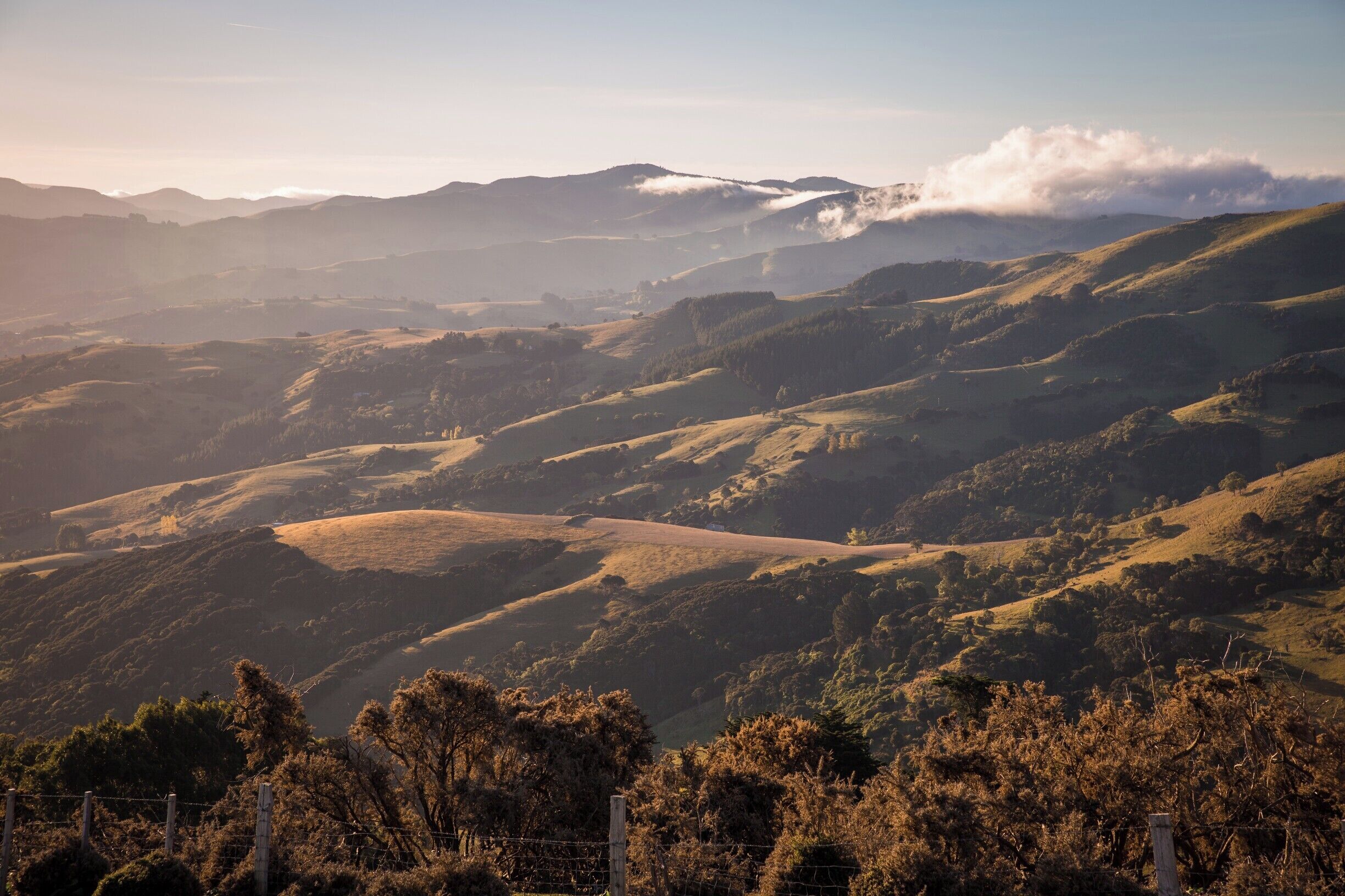 Rolling hills, a valley, and distant mountains with a fence in the foreground.
