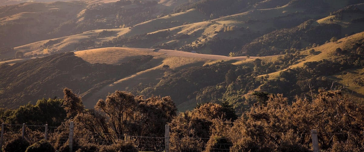 Rolling hills, a valley, and distant mountains with a fence in the foreground.