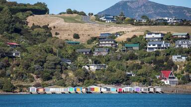 Un pueblo costero con casas móviles coloridas junto al agua, rodeado de colinas y viviendas.