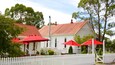 Een wit gebouw met een rood dak, omringd door een witte picket fence, en rode parasols ervoor.