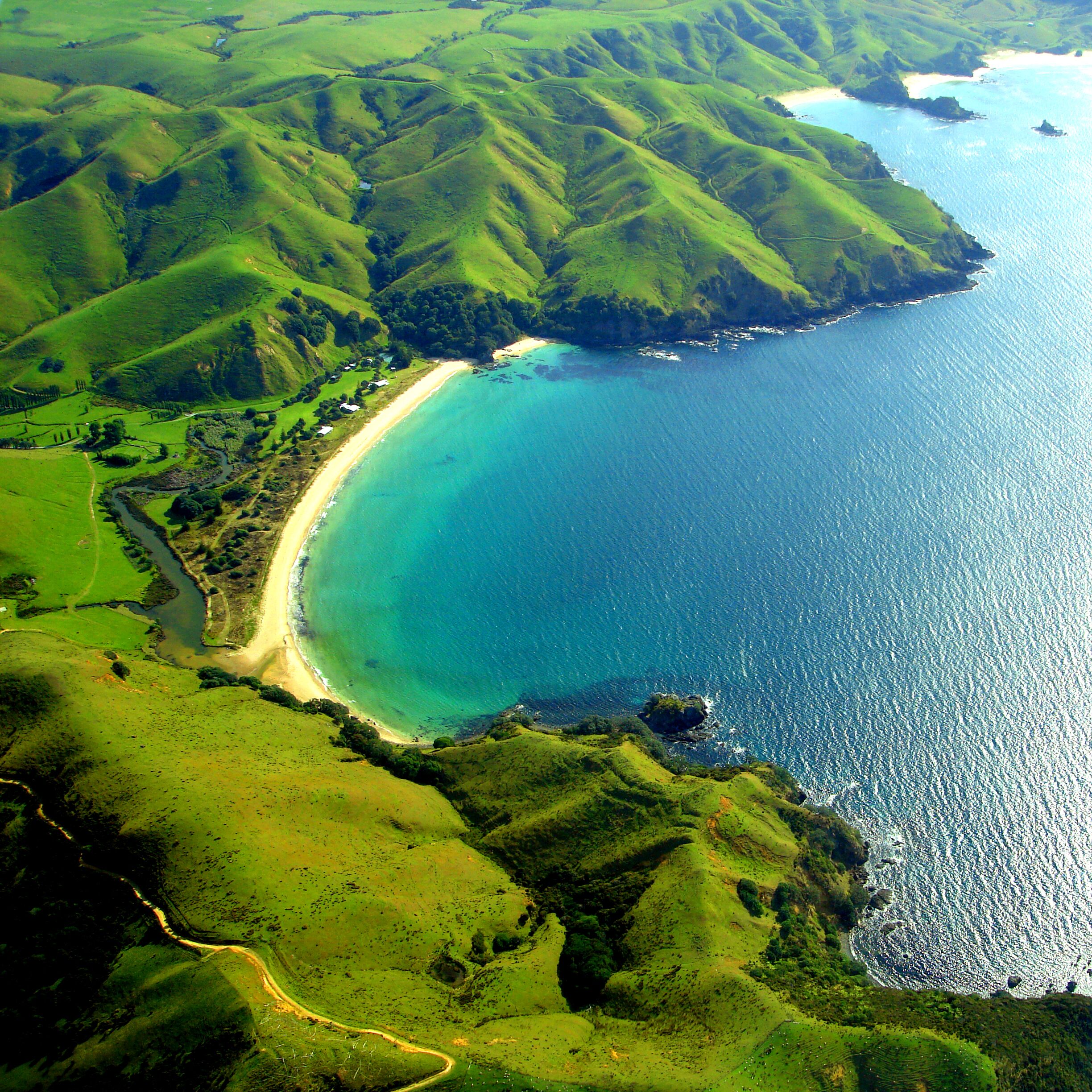 A coastal landscape with rolling hills, a sandy beach, and a clear blue sea.