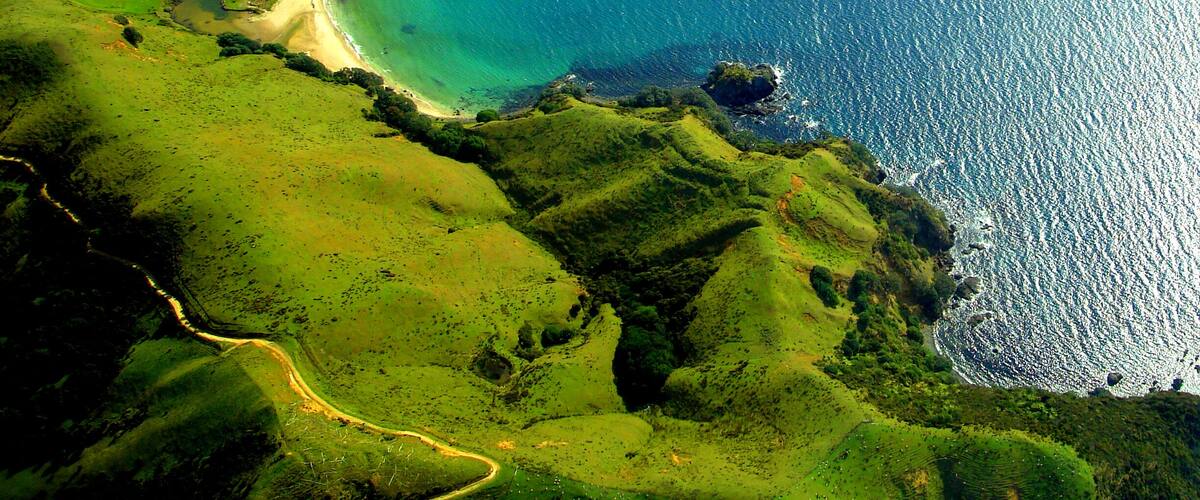 A coastal landscape with rolling hills, a sandy beach, and a clear blue sea.