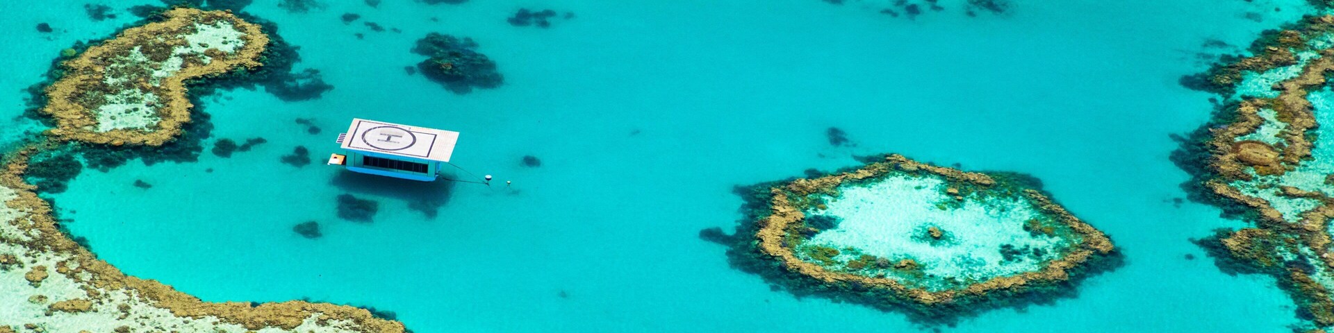 An aerial view of a turquoise lagoon with coral formations and a small building with a helipad.