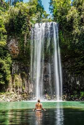 Ein Wasserfall stürzt in ein klares Becken, umgeben von dichtem Grün und steilen Felswänden.